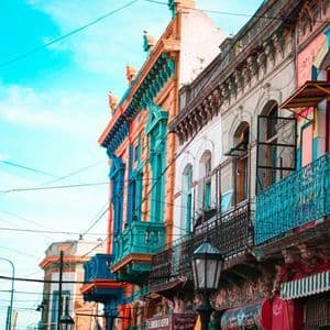 A low-angle view of brightly colored buildings with ornate balconies against a vibrant blue sky with crossing power lines.