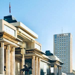 Un grande edificio con colonne e statue equestri si erge davanti a un moderno grattacielo sotto un cielo limpido.
