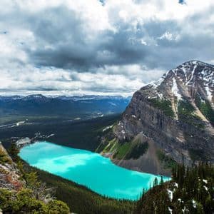 Una vista sopraelevata di un lago turchese brillante circondato da una pineta e una grande montagna rocciosa con chiazze di neve.