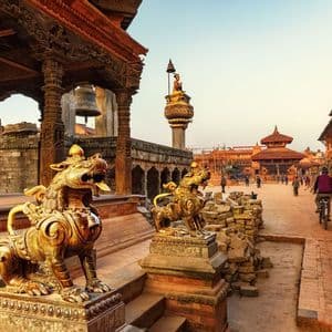 Due statue di leoni dorati su piedistalli custodiscono un complesso di templi storico con strutture in legno intagliato e persone che passeggiano.