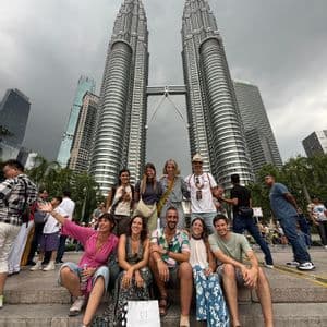 Un viaggio di gruppo WeRoad in posa per una foto sui gradini davanti a imponenti grattacieli gemelli sotto un cielo nuvoloso.