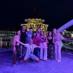 Un viaje en grupo de WeRoad posando para una foto en un puente moderno por la noche, con un gran edificio iluminado de fondo.