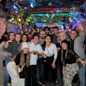 Un grupo de WeRoad posa para una foto, con bebidas en un bar decorado con luces de colores y bolas de discoteca.