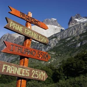 Un panneau de sentier en bois indiquant les directions vers Frances et Italiano, avec en toile de fond les montagnes escarpées de Paine Grande sous un ciel bleu.
