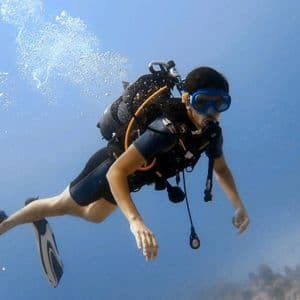 Un plongeur sous-marin équipé de tout son matériel, y compris un masque et des palmes, nage horizontalement dans une eau bleue claire.