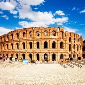 Die Ruinen eines großen, runden Steinamphitheaters stehen unter blauem Himmel mit weißen Wolken, mit Menschen im Vordergrund.