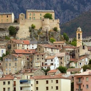 Ein befestigtes Dorf mit terrakottagedeckten Häusern und einem Glockenturm, auf einem felsigen, bewaldeten Berghang erbaut.