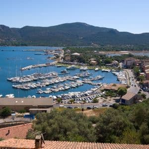 Luftaufnahme eines Hafens, gefüllt mit festgemachten Yachten und Segelbooten, umgeben von einer Küstenstadt und Bergen.