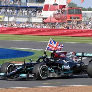 A black Formula 1 race car with a British flag attached drives around a track in front of spectators in the stands.