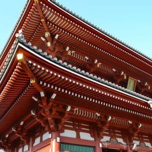Un'inquadratura dal basso dell'intricato tetto in legno dipinto di rosso di un tradizionale tempio giapponese, contro un cielo azzurro e limpido.
