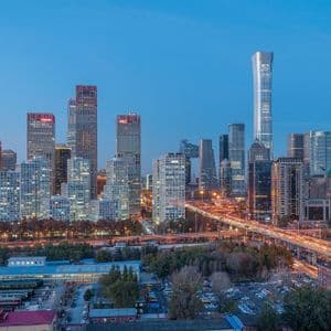 Uno skyline cittadino moderno con grattacieli illuminati e un'autostrada trafficata con scie luminose dal traffico al tramonto.