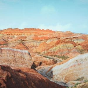 Un vasto paesaggio di montagne colorate e stratificate con sfumature di arancione, rosso e giallo sotto un cielo azzurro chiaro.