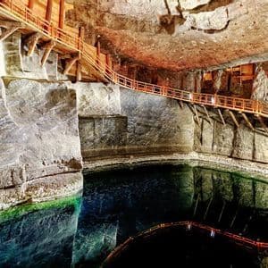 Une passerelle en bois illuminée longe les parois rocheuses ciselées d'une grotte, surplombant un lac souterrain sombre et immobile.