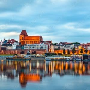Une ville européenne historique avec une grande cathédrale est illuminée au crépuscule, ses édifices et lumières se reflétant dans la rivière.