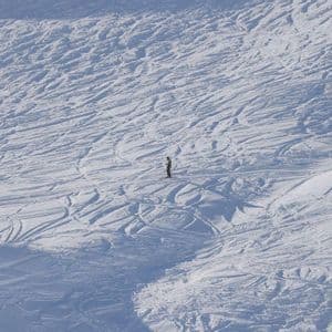Uno snowboarder solitario su un vasto pendio innevato e tracciato.