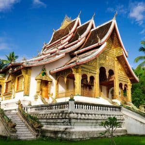 Un temple orné blanc et or avec un toit à plusieurs niveaux, entouré de palmiers luxuriants sous un ciel bleu éclatant.