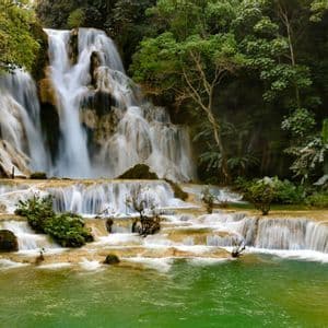 Une cascade à plusieurs niveaux dévale des bassins de travertin pour se jeter dans un lagon vert, entourée d'une jungle luxuriante.