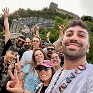 Un gruppo WeRoad sorride e si mette in posa per un selfie su una grande cinta muraria storica che si snoda in un paesaggio verde e collinare.