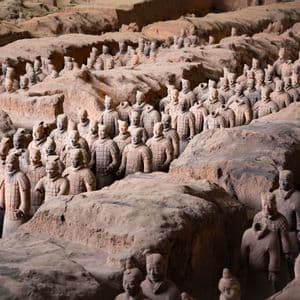 Numerose statue di guerrieri in terracotta a grandezza naturale disposte in file ordinate all'interno di trincee di terra scavate.
