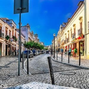 Una vista dal basso di una strada acciottolata fiancheggiata da edifici bianchi e negozi sotto un cielo limpido e azzurro intenso in una città europea.