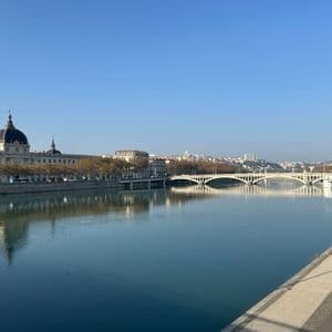 Une large rivière traverse une ville par une journée ensoleillée, avec un bâtiment en dôme sur une rive et un pont arqué au loin.