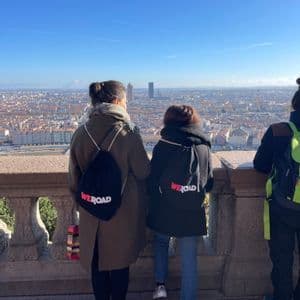 Drei Personen einer WeRoad Gruppenreise, von hinten gesehen, blicken an einem sonnigen Tag von einer steinernen Balustrade auf eine Stadtlandschaft.