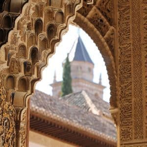 Primer plano de un arco ornamentado con tallas detalladas, enmarcando una vista de una torre y un tejado de tejas al fondo.