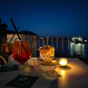 Due cocktail all'arancia e stuzzichini su un tavolo illuminato da una candela su una terrazza con vista mare di notte.