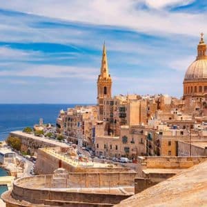 Una città costiera con cupola e campanile di chiesa si affaccia sul mare blu sotto un cielo parzialmente nuvoloso.