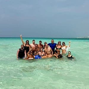 Un groupe WeRoad prend la pose pour une photo, debout dans l'eau claire et turquoise de l'océan, sous un ciel gris.