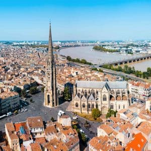 Vue aérienne d'une ville européenne historique avec une grande cathédrale gothique, des toits en terre cuite et un large fleuve en arrière-plan.