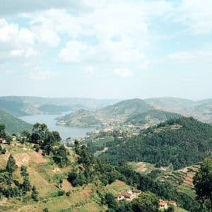 Ein Panoramablick auf grüne, terrassierte Hügel und Täler, die einen großen, sich schlängelnden See unter einem teilweise bewölkten Himmel umgeben.