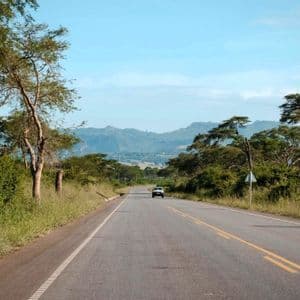 Ein weißer SUV fährt auf einer asphaltierten Straße durch eine ländliche Landschaft mit üppig grünen Bäumen und Hügeln in der Ferne.