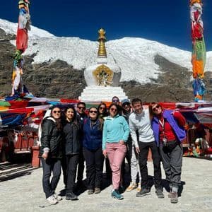 Un viaggio di gruppo WeRoad posa per una foto davanti a uno stupa bianco e bandiere di preghiera, con una montagna innevata sullo sfondo.