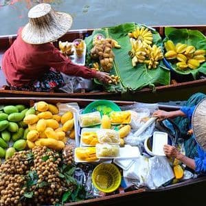 An overhead view of two vendors in conical hats selling fresh tropical fruits like bananas and mangoes from their boats at a floating market.