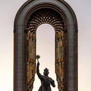 Una statua di bronzo di un re incoronato che alza uno scettro, incorniciata in un grande arco sontuoso sormontato da una corona.