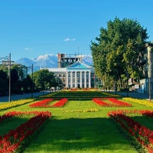 Un parco curato con aiuole di fiori rossi e gialli che conduce a un edificio classico con montagne innevate sullo sfondo.