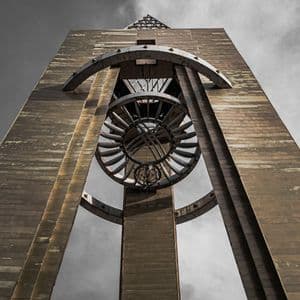 Una ripresa dal basso di un'alta torre di cemento con una grande sfera armillare metallica sospesa contro un cielo coperto.