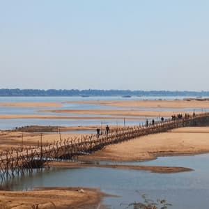 Un gruppo WeRoad attraversa un lungo e rustico ponte di bambù su un ampio fiume sabbioso sotto un cielo limpido.