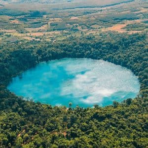 Veduta aerea di un lago craterico circolare turchese, circondato da una fitta foresta verde.