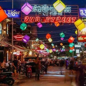 Una vivace strada notturna è illuminata da una grande insegna al neon 'Pub Street' e da colorate lanterne a forma di cubo appese in alto.