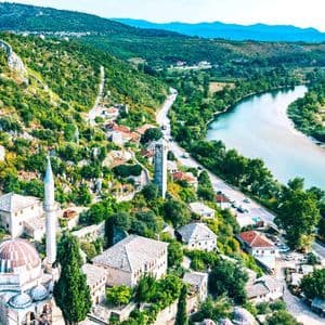 Eine Luftaufnahme einer historischen Stadt mit einer Moschee und einem Uhrturm, gebaut auf einem grünen Hügel neben einem gewundenen Fluss.