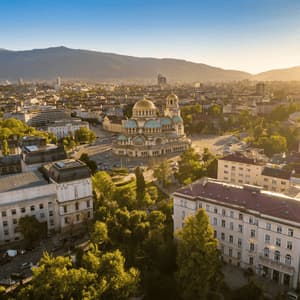 Vista aérea de una extensa ciudad, con una gran catedral de cúpulas doradas en el centro y montañas de fondo al atardecer.