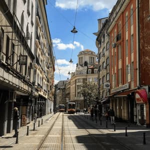 Un tranvía recorre una calle de la ciudad con vías entre edificios altos y clásicos bajo un cielo azul con nubes.