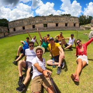 Eine WeRoad Gruppenreise macht ein Selfie, während sie auf einem Rasen vor antiken Steinruinen sitzen.