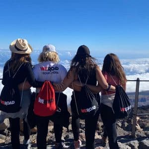 Un voyage de groupe WeRoad de quatre femmes, bras dessus bras dessous, contemplant une mer de nuages depuis le sommet d'une montagne.