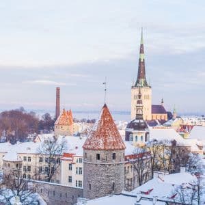 Uno skyline di una città storica in inverno, con tetti coperti di neve, torri di pietra con tetti rossi e un'alta guglia di chiesa.