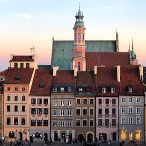 Edificios coloridos y tradicionales y la torre de una catedral en una plaza histórica al atardecer.