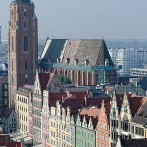Una vista aérea de una plaza de ciudad europea con coloridos edificios históricos y una gran torre de iglesia de ladrillo al fondo.