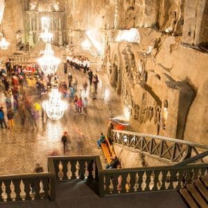 Vista aérea y de larga exposición de personas en una vasta cámara subterránea excavada en roca, iluminada por grandes candelabros.